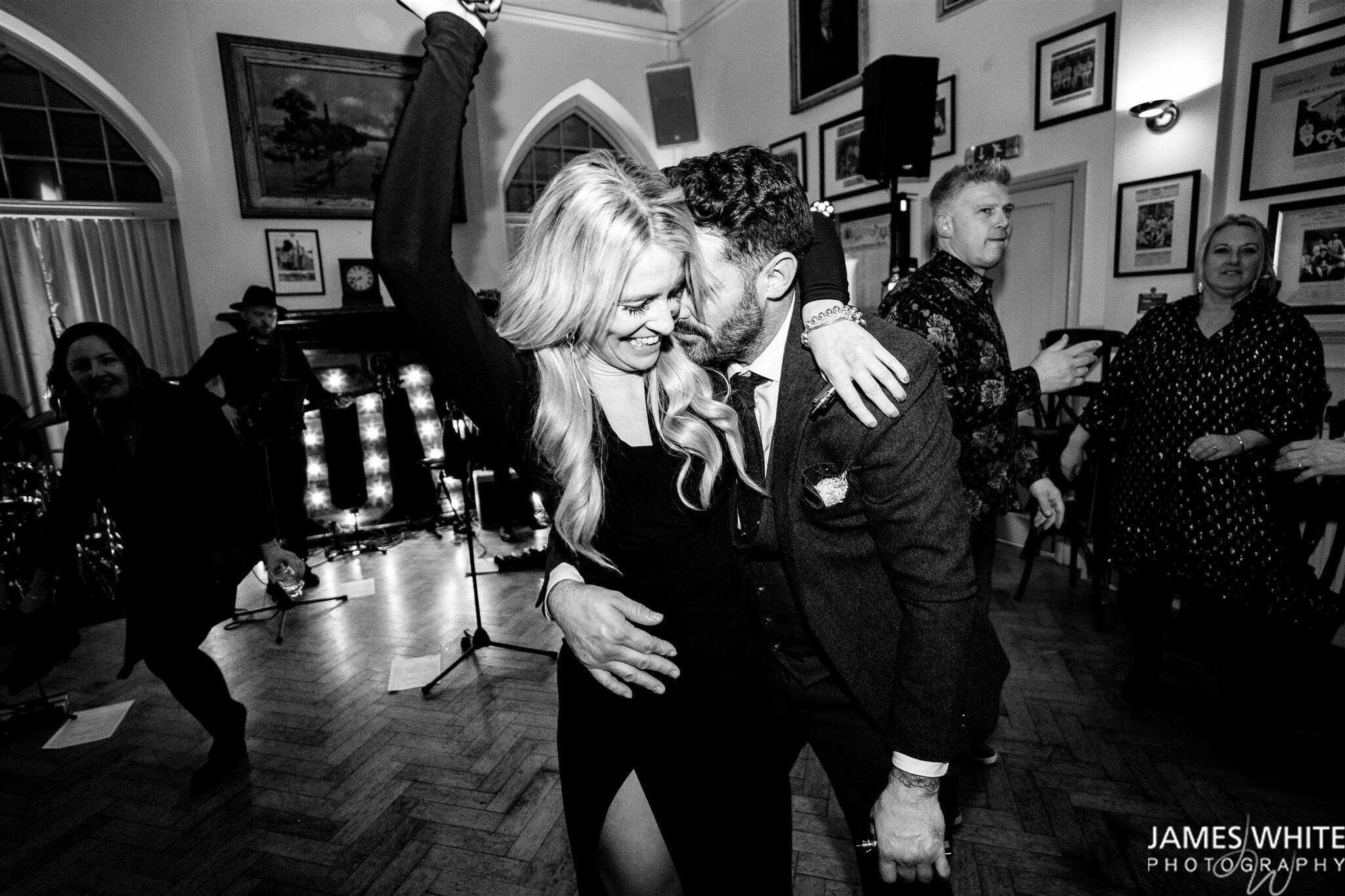 Couple dancing together at a wedding party with live entertainment in black and white