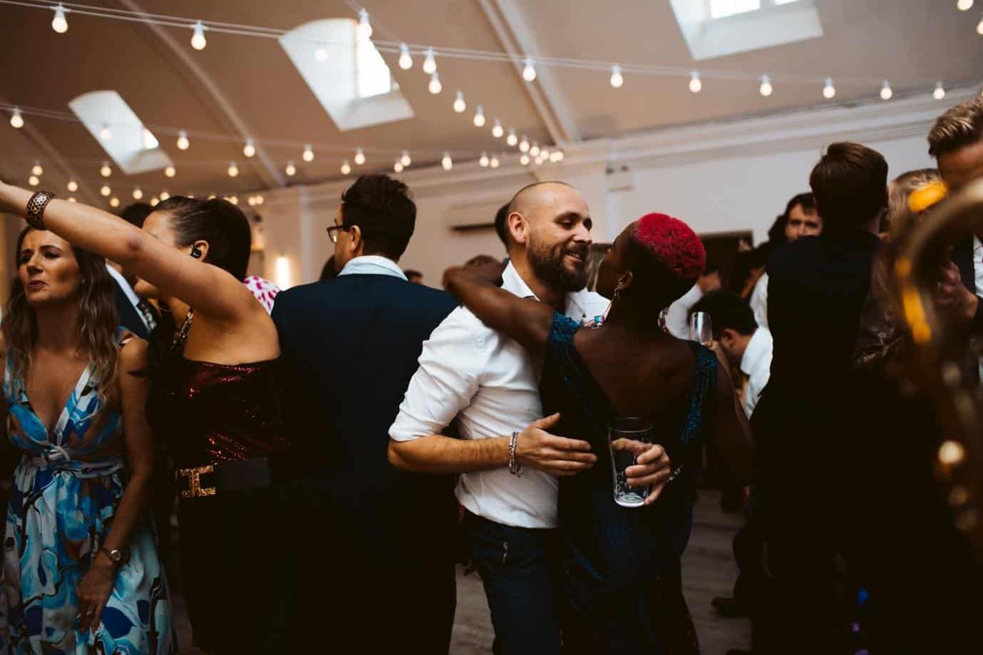 Guests dancing and celebrating at a packed wedding reception venue with string lights