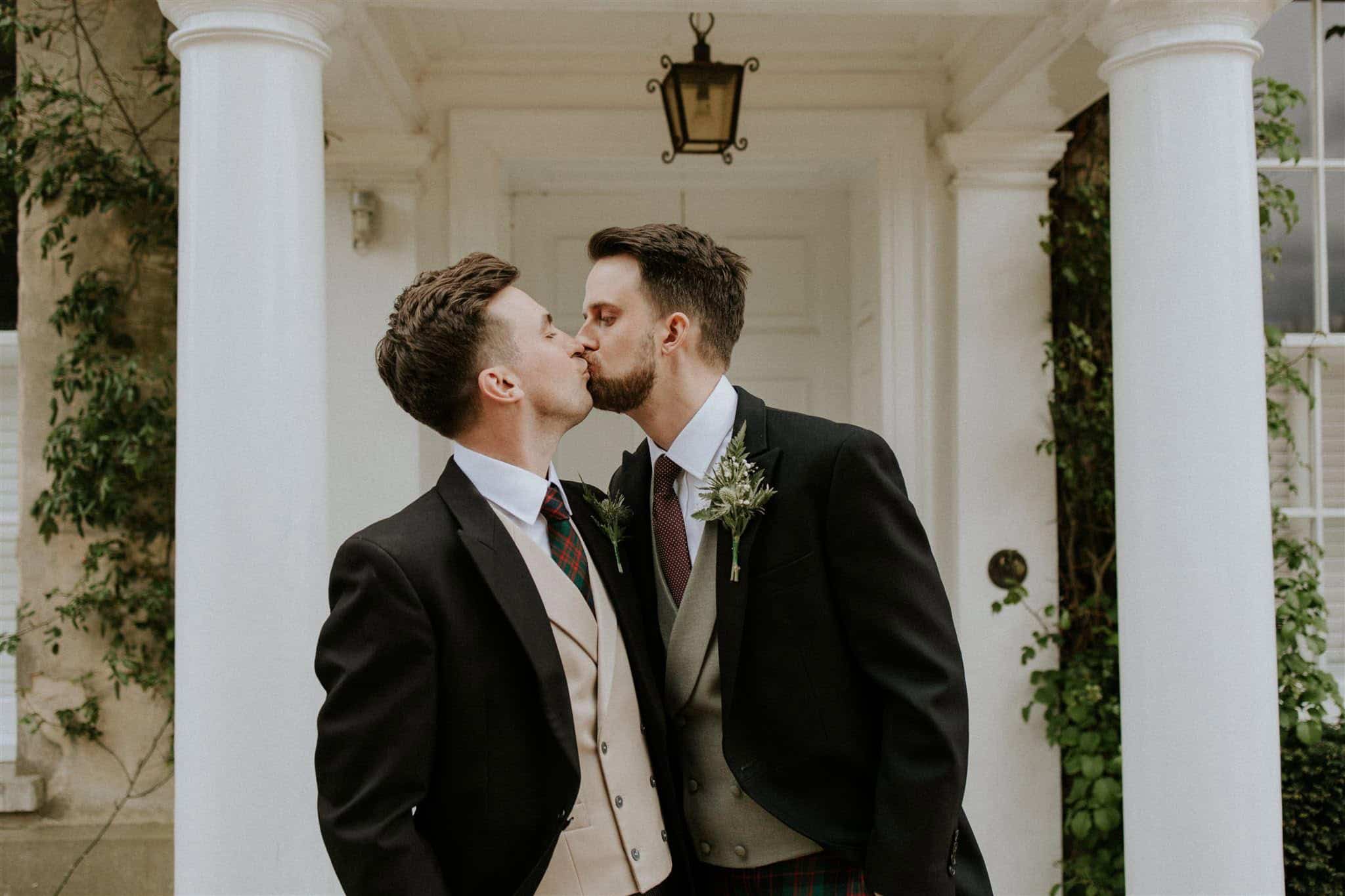 Same-sex couple sharing a wedding kiss outside a country house wedding venue